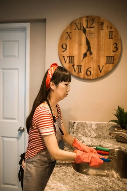 Two women in work clothes cleaning a modern living room using a vacuum and mop.